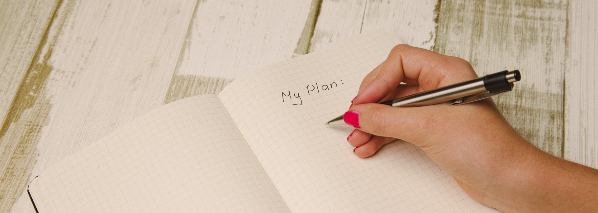 A planner is on a desk, opened to a page that has "My Plan:" handwritten. A women's hand is visible and is about to write on the page.